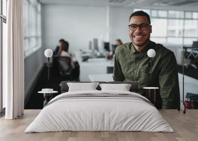 portrait of a successful smiling young professional businessman sitting over desk in front of collea Wall mural