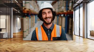 Portrait of happy male worker in warehouse wearing orange vest and white helmet standing between shelves Wall mural