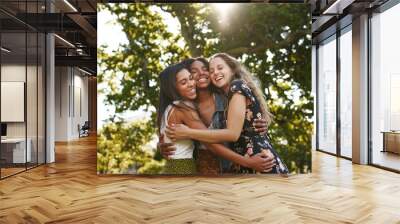 Portrait of happy three multiethnic multiracial female friends closely hugging and showing care and love for each other in park Wall mural