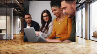 Smiling diverse friends social networking on a laptop computer grouped together reading the latest information on the screen Wall mural