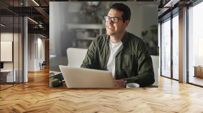 Smiling man with laptop sitting at desk looking away Wall mural