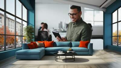 Smiling young businessman touching smartphone and checking online information in the modern office Wall mural