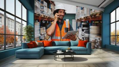 Successful factory manager tracking dispatch details using digital tablet while in conversation over smartphone in warehouse Wall mural