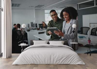 Successful two african american young businesspeople sitting on desk using digital tablet while colleague in background at office  Wall mural