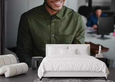 Thoughtful smiling young businessman holding digital tablet looking away while sitting at his working place in office Wall mural