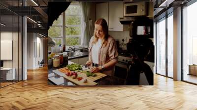 Woman in modern kitchen chopping fresh green vegetables to record food recipe on vlog - young woman vlogging in isolation  Wall mural