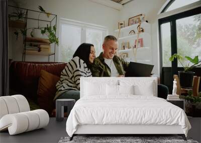 Young couple sitting on the couch looking at a laptop - 2 people streaming from their laptop Wall mural