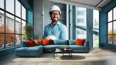 Smiling engineer holding hardhat and standing near window in office  Wall mural