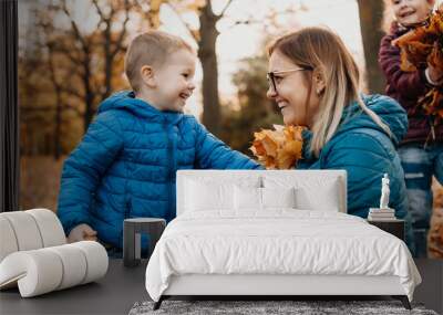 Cheerful caucasian mother playing with her kids while they are bringing autumn colorful leaves Wall mural