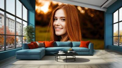 Close up portrait of a red hair woman girl with freckles looking at camera laughing over the shoulder against sunset outside. Wall mural