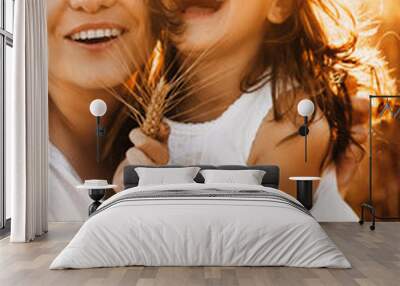 Close up portrait of lovely daughter and her mother embracing and laughing against sunset in a wheat field. Wall mural