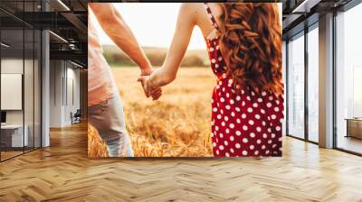 Close-up view of a couple's hands holding each other as they walk through the wheat field, the boyfriend taking his girlfriend to a secret place, he prepared a Wall mural