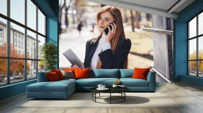 Confident smiling business woman talking on mobile phone waiting for business meeting in a summer park. Attractive beautiful girl. Marketing technology Wall mural