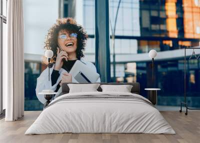 Curly haired caucasian woman is having a business discussion while holding her laptop and looking through eyeglasses Wall mural