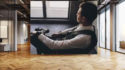 Elegant man dressed in a suit  sitting on a chair and looking through window. Wall mural