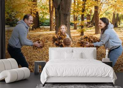 Family with piles of maple leaves having fun in forest throwing up leaves into each other. Concept autumn, yellow leaves, autumn mood. Happy family outdoors Wall mural