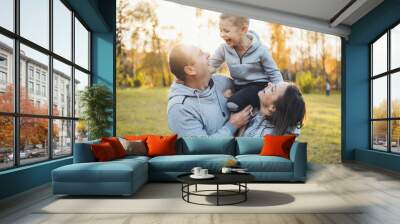 Happy family of mother and father carrying their boy child on shoulders. Smiling happy child. Positive person. Wall mural