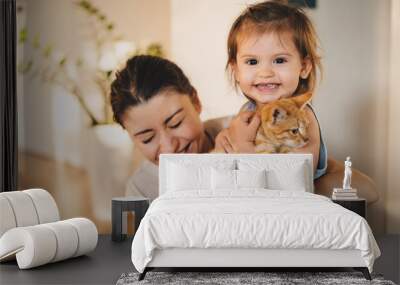 Mother with her baby playing with pet on the floor at the living room at home, smiling looking at camera, having fun together. Fun play together. Smile emotions Wall mural