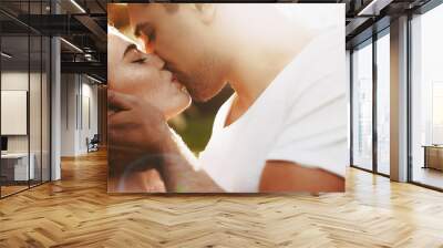 Portrait of a amazing young red haired woman kissing with her boyfriend with closed eyes against sunrise while man is touching her face. Wall mural