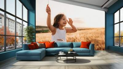 Smiling caucasian girl dressed in white dress is walking in a wheat field with a cheerful smile on leaps Wall mural