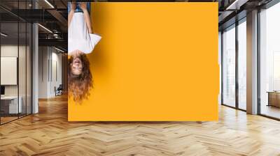 Upside down photo of a caucasian woman in white shirt and jeans smiling on a yellow studio wall with free space Wall mural