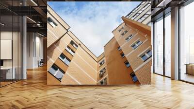 Look up at the modern multistory apartment building of beige brick against the cloudy sky. Wall mural