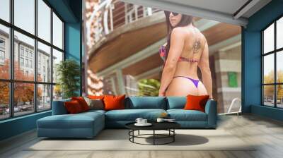 Back bottom view of sexy brunette woman wearing colorful bikini and sunglasses standing by the pool. Summer, outdoors shot Wall mural