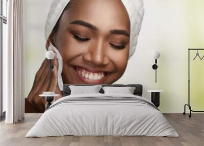 Close-up portrait of a beautiful smiling woman with clean skin cleaning her face with cotton swab pad isolated on bright background. Beauty treatments and cosmetics spa therapy Wall mural