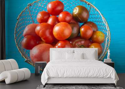 Various of organic tomatoes in vintage metallic basket on blue paint wooden background. Summer gardening, vegan food concept Wall mural