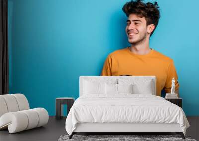 A cheerful young man in casual attire, holding a coffee cup and looking off to the side with a relaxed smile, isolated on a solid pastel blue background  Wall mural