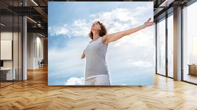 breathing outside - zen middle aged yoga woman opening up her chakra with arms raised,practicing meditation for freedom over summer blue sky,low angle view Wall mural