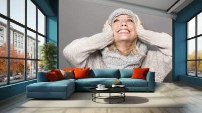 lovely young woman with blonde hair wearing winter hat and clothes, looking up with hands on ears for fun and happiness Wall mural