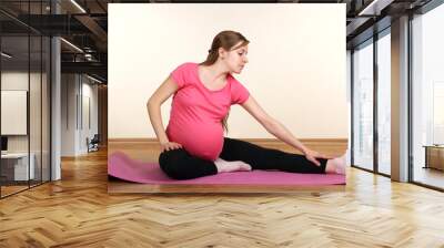 pregnant woman sitting on yoga mat and performs warm-up on white background Wall mural