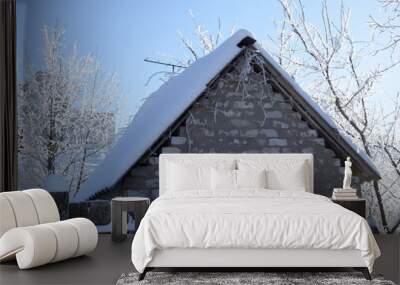 Snow covered tree branches above the snowy roof of a brick building with a blue sunny sky Wall mural