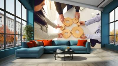 A group of business people holds wooden wheels with teeth in their hands on an office white table. Wall mural