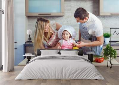 A happy family prepares food from vegetables in the kitchen. Wall mural