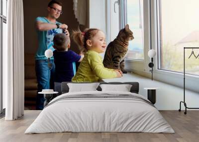 A happy family. Little  girl looks out the window on  background of her family. Wall mural