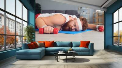 A lazy fat man lies with dumbbells on the floor of the house. Wall mural