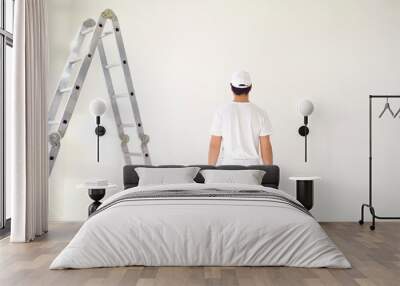 A male painter in a white uniform with a roller works in his hand in a white room Wall mural