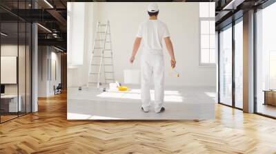 A male painter in a white uniform with a roller works in his hand in a white room Wall mural