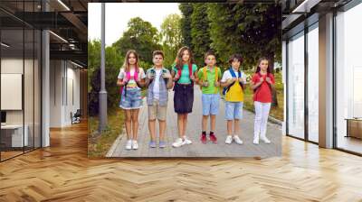 Back to school concept. Group of children with school bags. Outdoor portrait of several kids with backpacks. Six happy elementary students standing on a park path together Wall mural