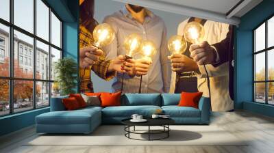 Background with young multiethnic business team holding glowing vintage Edison lightbulbs. Multiracial men and women join shining electric light bulbs for teamwork and sharing creative ideas Wall mural