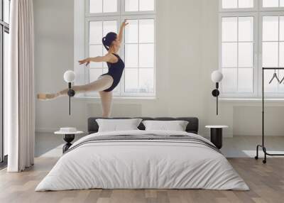 Ballerina. Young graceful ballet dancer is rehearsing a performance in a white studio with windows. Wall mural