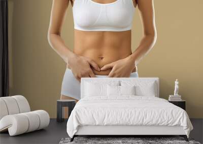 Banner with cropped shot of beautiful young woman in white underwear standing against beige background and holding hands on her stomach area. Health, constipation, menstruation, period cramps concept Wall mural