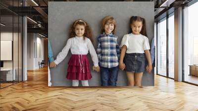 Banner with portrait of happy little kids in casual wear. Group of adorable children in new neat clothes holding hands, smiling and looking at camera standing together against grey studio background Wall mural