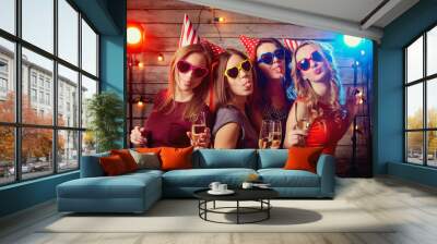 Birthday party girlfriends. Beautiful girls in caps, and colored glasses with champagne glasses grimace shows language. Wall mural