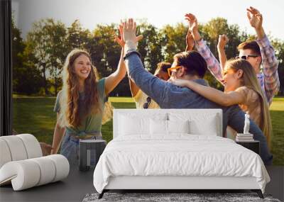 Bunch of happy young friends all together having fun on warm sunny day in summer park. Diverse group of cheerful joyful positive people standing on green lawn, smiling and giving each other high five Wall mural