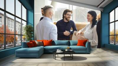 Business colleagues having fun chatting and discussing work in casual conversation in office. Beautiful business men and woman in stylish business attire smiling joking and discussing work. Wall mural