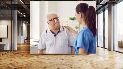 Caring medical nurse comforting senior patient in office. Side view of female doctor caregiver wearing uniform supporting elderly man. Empathy, healthcare and support concept Wall mural