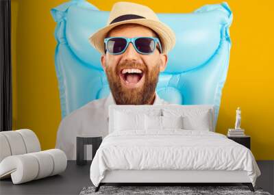 Cheerful handsome bearded business man in office shirt, tie, sunhat and sunglasses with inflatable beach water mattress laughs happily and has fun on summer holiday trip. Isolated on yellow background Wall mural